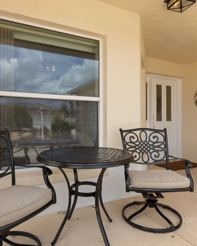 Covered patio with black ornamental metal chairs, round table, and large window overlooking landscape