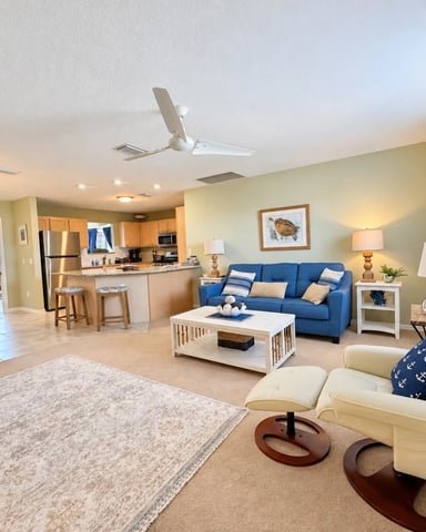 Open-plan living room with cream armchair, blue sofa, white coffee table, and kitchen with stainless steel appliances in background
