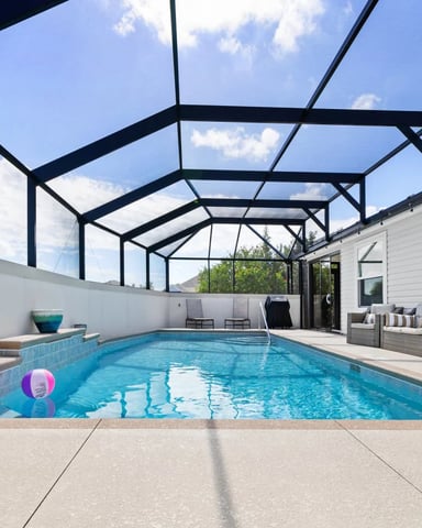 Enclosed swimming pool with glass roof, concrete deck, white walls, and lounge seating area beside modern house