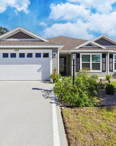 Single-story ranch home with white garage, gray siding, and landscaped front yard under blue sky