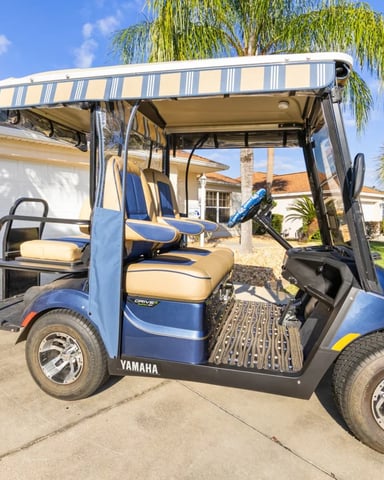 Blue and tan golf cart with striped canopy parked in driveway of residential home with garage and palm trees