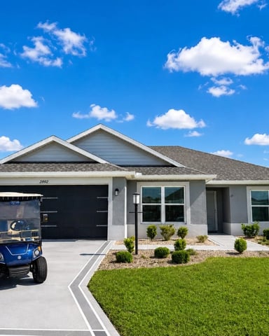 Single-story gray house with black garage door, landscaped front yard, and blue golf cart in driveway under clear blue sky