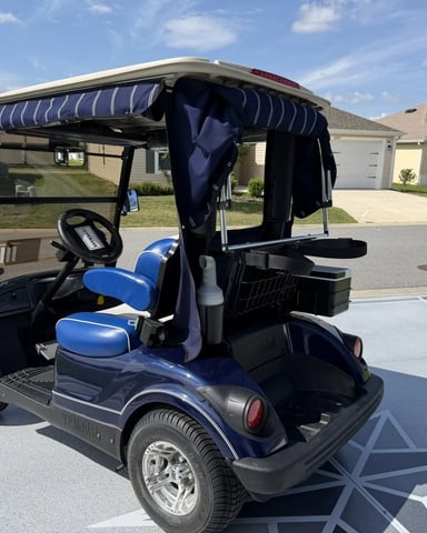 Blue and black golf cart with striped canopy parked in residential driveway